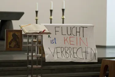 Altarraum einer Kirche, am Altar hängt ein großes Transparent mit der Aufschrift "Flucht ist kein Verbrechen"