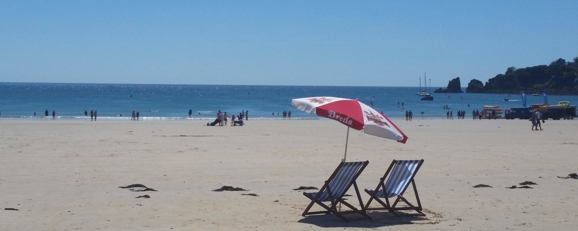 Zwei leere Liegestühle und ein Sonnenschirm am Strand.